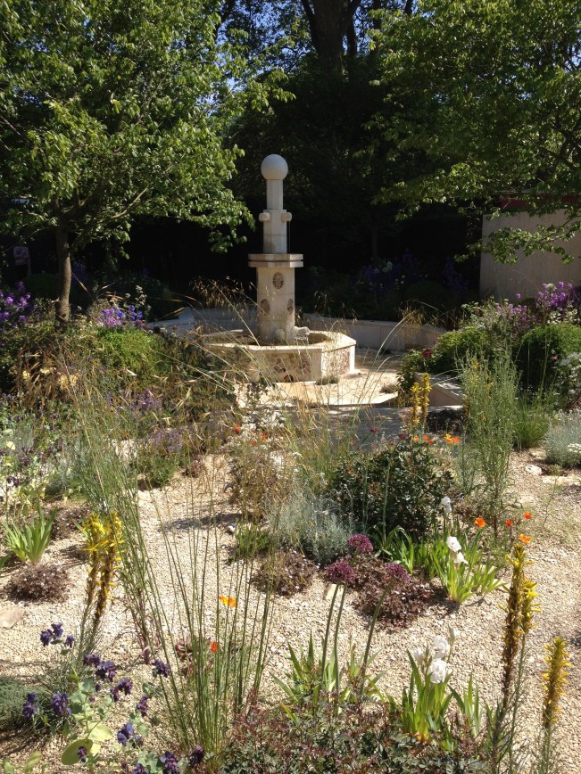 M&G Investments is the show sponsor of the RHS Chelsea Flower Show; their garden, designed by Cleve West, is based on ancient Persian garden designs but with a modern twist. The design is divided into the traditional four quartered sections with a sunken central carved stone fountain and four watery rills. The yew hedges and carved limestone panel  behind the fountain provide the feeling of an enclosed oasis. Plants to the left are of the blues and purples and to the right there is jellybean-colored floral display set in an arid, pebbly area suggesting the geographic home of  the original design inspiration. As usual Cleve West does not disappoint. His design and plantings pack a horticultural punch to whisk the visitor away to what I was going to call warmer climes- but today I cannot do that as the day was sunny. bright and downright hot at times. A perfect way to begin Chelsea Flower Show week. @RHSChelseaFloweShow