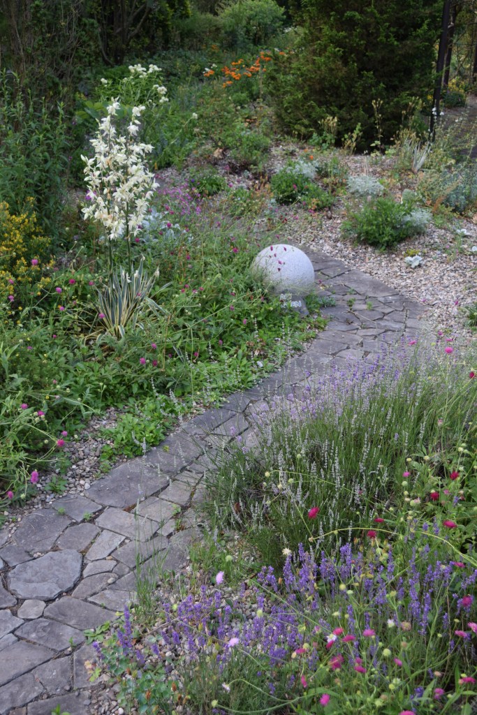 View from above of a stone path surrounded by flower-filled beds mulched with gravel