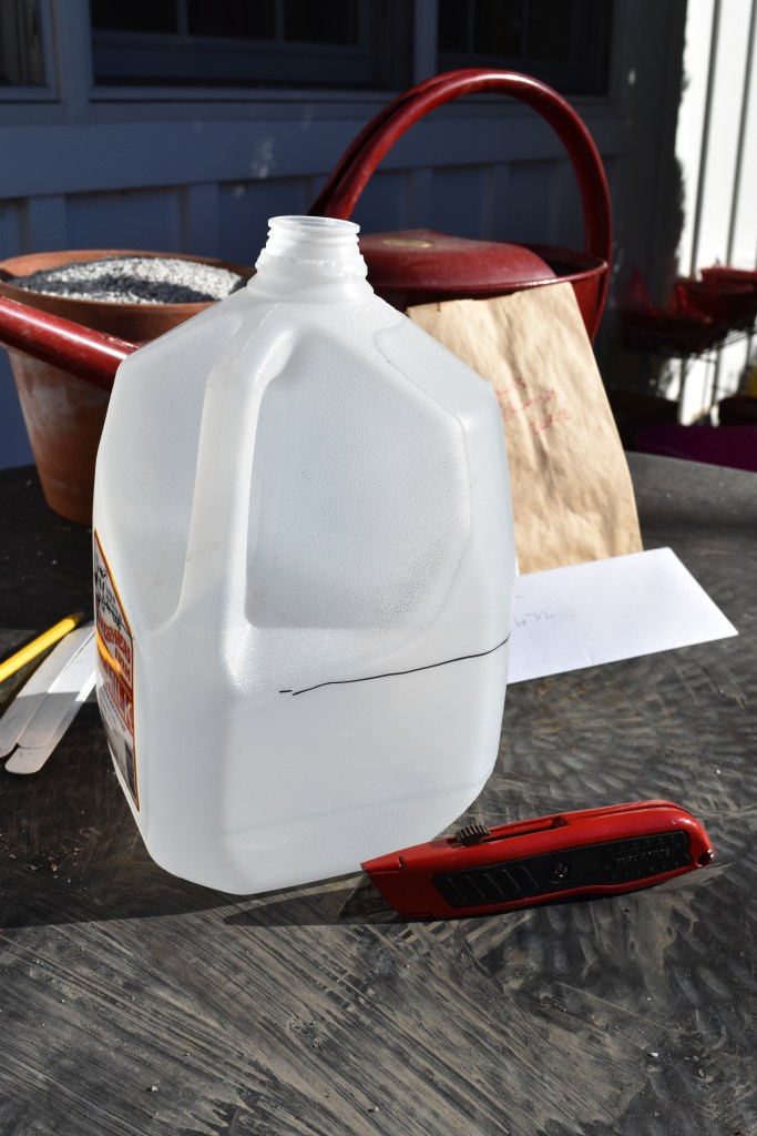 An empty plastic milk container with a line on it about on third of the way up. A retractable blade knife is ready to cut along the line.