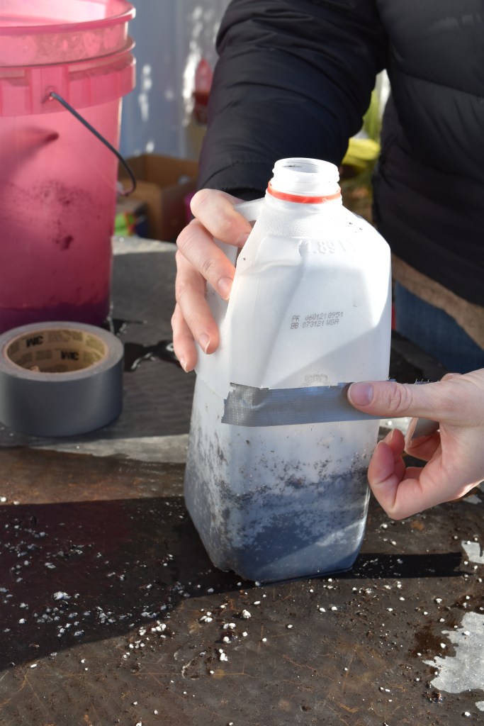 A person sealing up a milk jug with duct tape after seeds have been planted inside