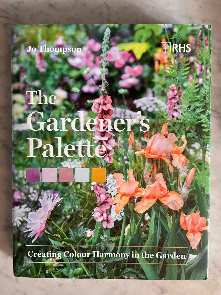 Gardening book front cover with coral and salmon colored verbascum spike, and bearded iris flowers against a garden background. There are color swatches below the title. The Gardener's Palette by Jo Thompson