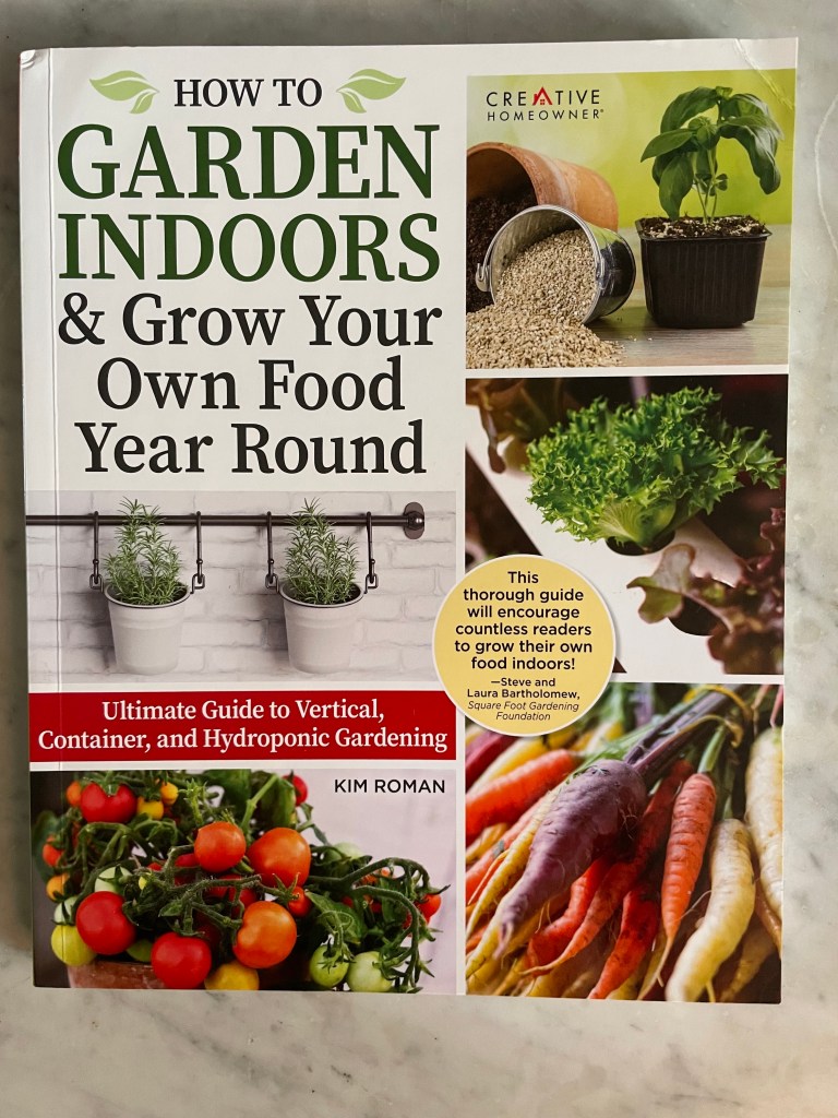 Front Cover of a gardening book about food gardening inside your house by Kim Roman. It shows colorful carrots, some herbs and vegetables some in pots.