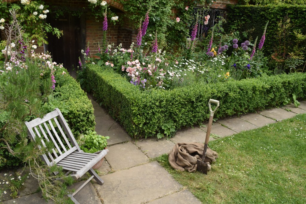 English garden with pink roses and foxgloves, shovel, and seat