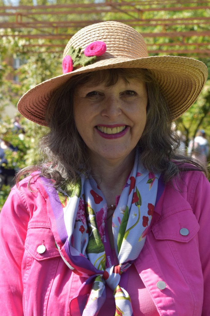 Jenny Rose Carey wearing a straw hat and flowers - with a pink jacket and scarf