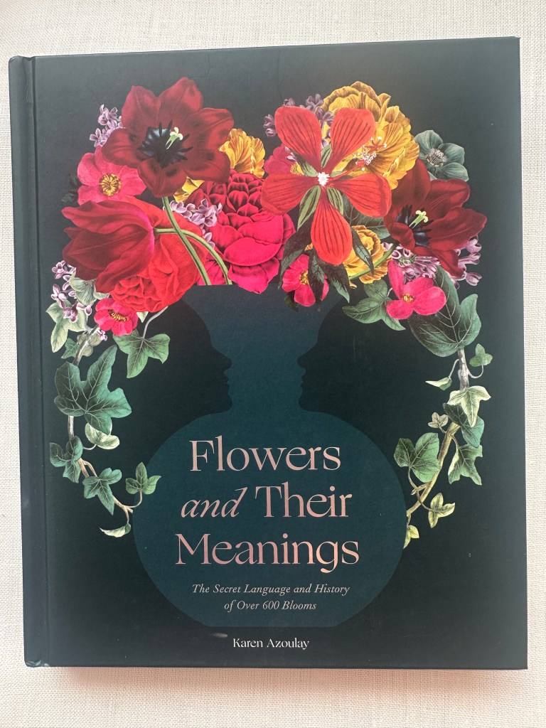 Book Cover of Flowers and Their Meanings by Karen Azoulay witha black background and a wreath of flowers and leaves including ivy. A vase in the middle seems to suggest two faces on the outside