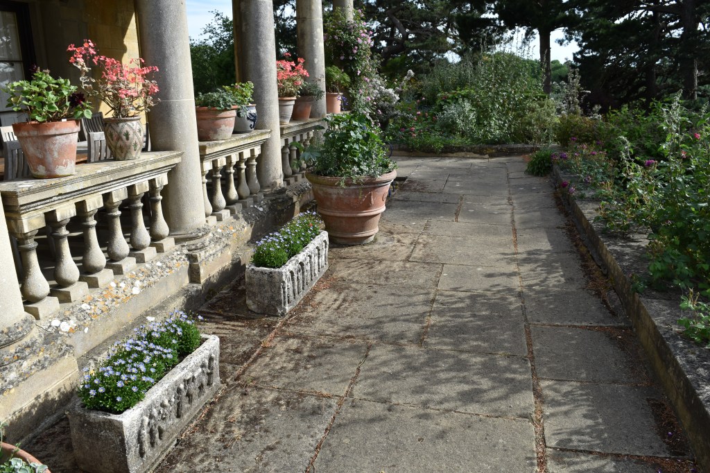 Kiftsgate Court terrace showing the color of the local limestone and potted geraniums and other plants.