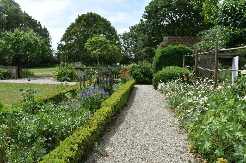The view down the path in the back garden at Kelmscott Manor. There is a low box hedge to the left and a cottage style planting to the right.