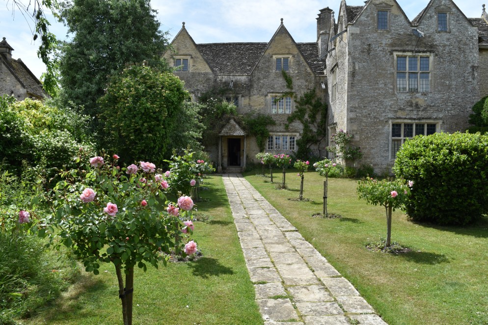 View of Kelmscott Manor looking down the front stone path flanked with standard roses