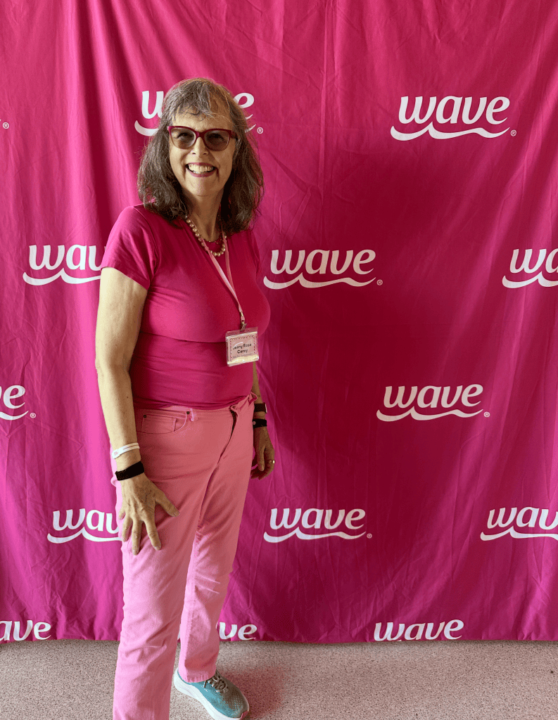 Jenny Rose Carey in her usual pink outfit in front of a Wave Petunia sign also in Pink.