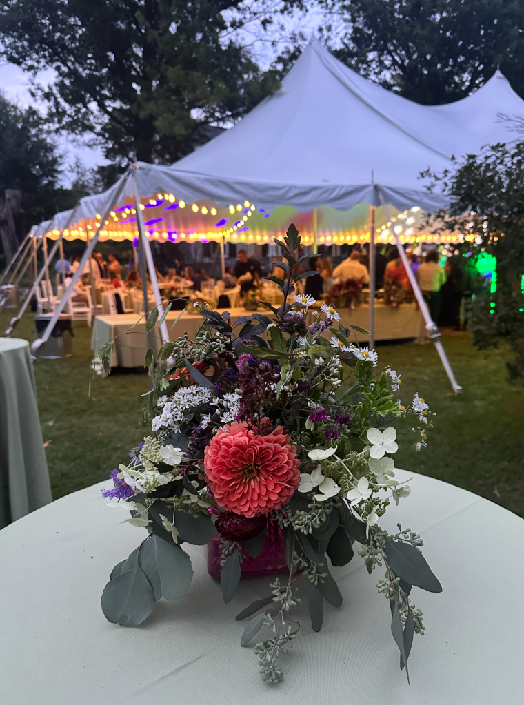Wedding tent on a lawn with flowers including an orangy zinnia on a high top table